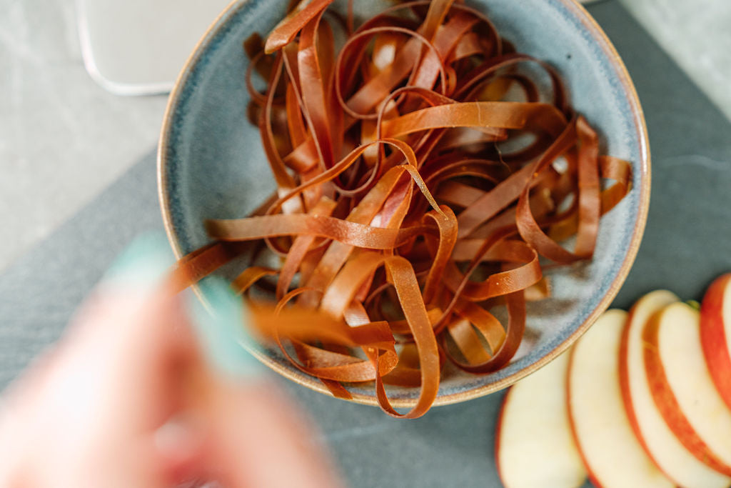 Auf einer Schieferplatte ist eine Schale mit Fruchtschlangen Sorte Mango sowie Apfelschnitze