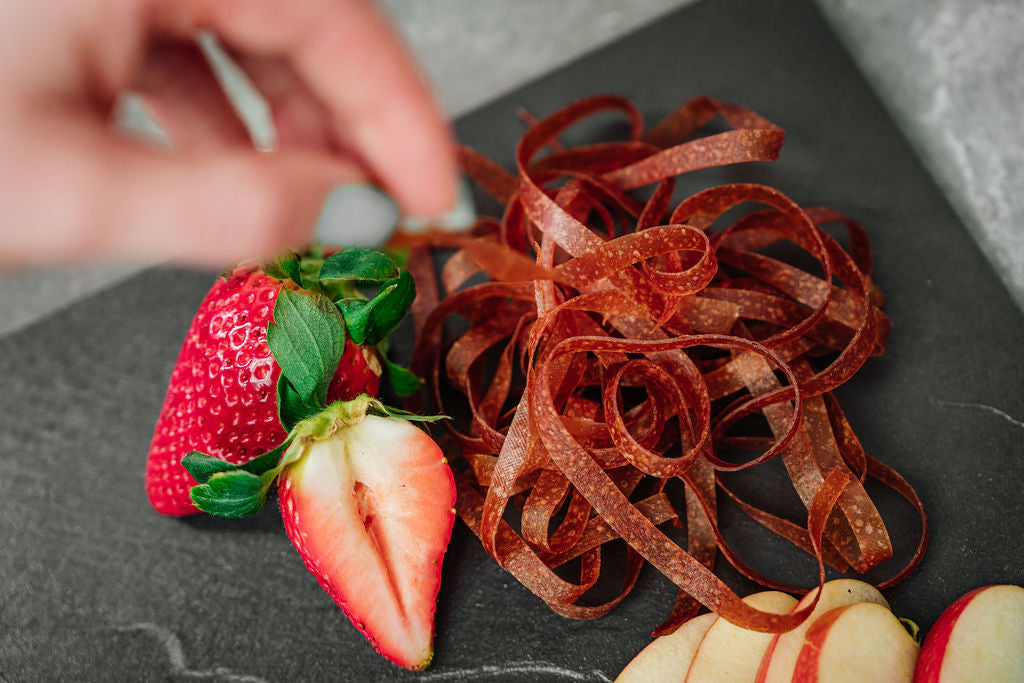 Auf einer Schieferplatte liegen Erdbeeren, Fruchtschlangen Sorte Erdbeere sowie Apfelschnitze