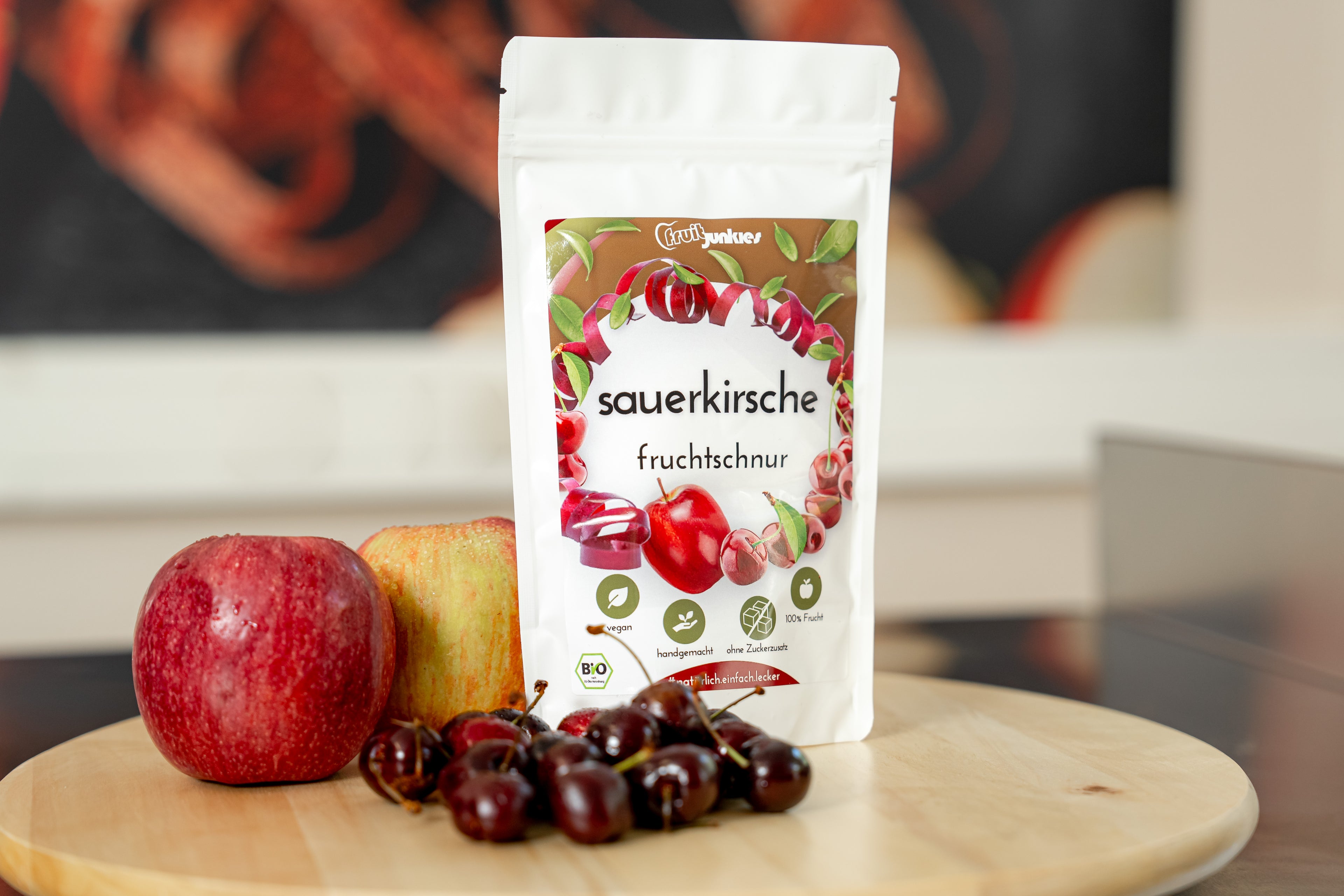 36g Sauerkirsch Tüte von fruitjunkies auf Holzdrehteller mit umliegenden Früchten Äpfel und Sauerkirsche